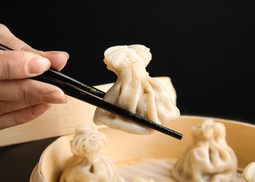 Photo of Woman cooking tasty baozi dumplings in bamboo steamer, closeup