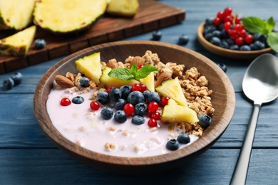 Image of Tasty granola with yogurt, berries and sliced pineapple served for breakfast on blue wooden table