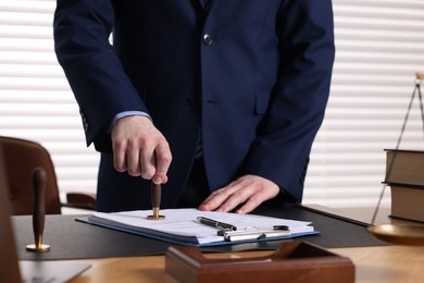 Photo of Notary stamping document at table in office, closeup