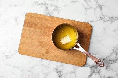 Saucepan with melting butter on marble background, top view. Space for text
