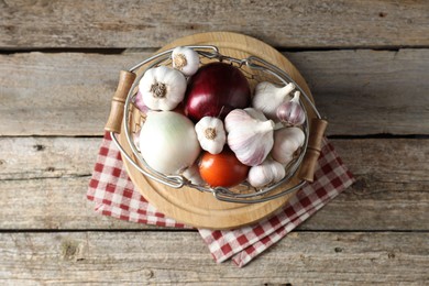 Photo of Fresh raw garlic and onions in metal basket on wooden table, top view