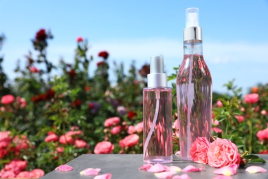 Photo of Bottles of facial toner with essential oil and fresh roses on table against blurred background. Space for text