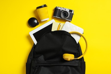 Photo of Stylish urban backpack with different items on yellow background, flat lay