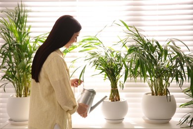 Photo of Young woman watering house plant on window sill indoors