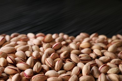 Many tasty pistachios on black background, closeup view