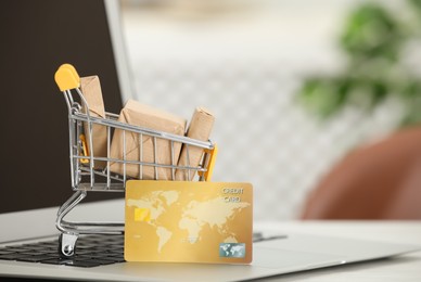 Photo of Online payment concept. Small shopping cart with bank card, boxes and laptop on table, closeup