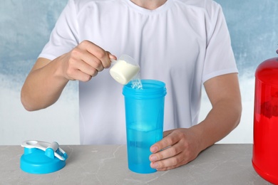 Photo of Man preparing protein shake with powder at table, closeup