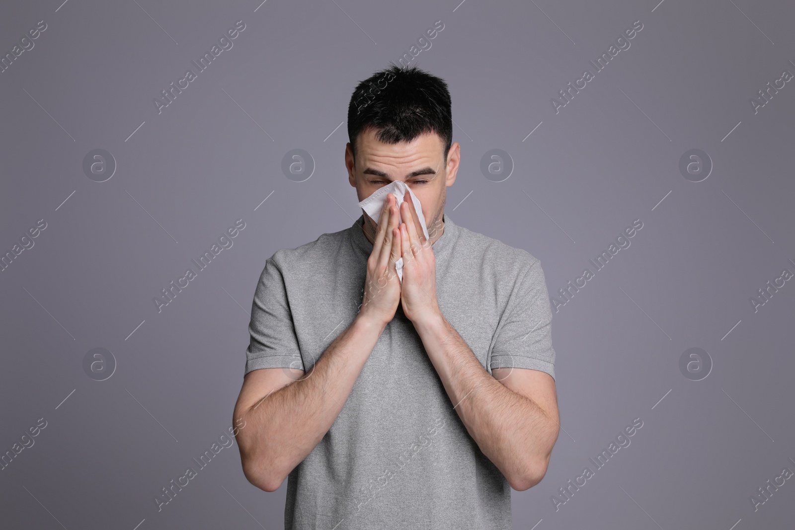 Photo of Young man blowing nose in tissue on grey background. Cold symptoms