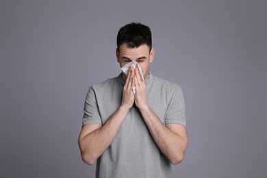 Photo of Young man blowing nose in tissue on grey background. Cold symptoms