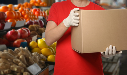 Image of Man with cardboard box against fresh fruits in store, closeup. Wholesale market