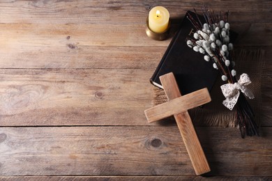 Photo of Burning church candle, cross, Bible and willow branches on wooden table, flat lay. Space for text