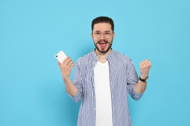 Emotional man with smartphone against light blue background