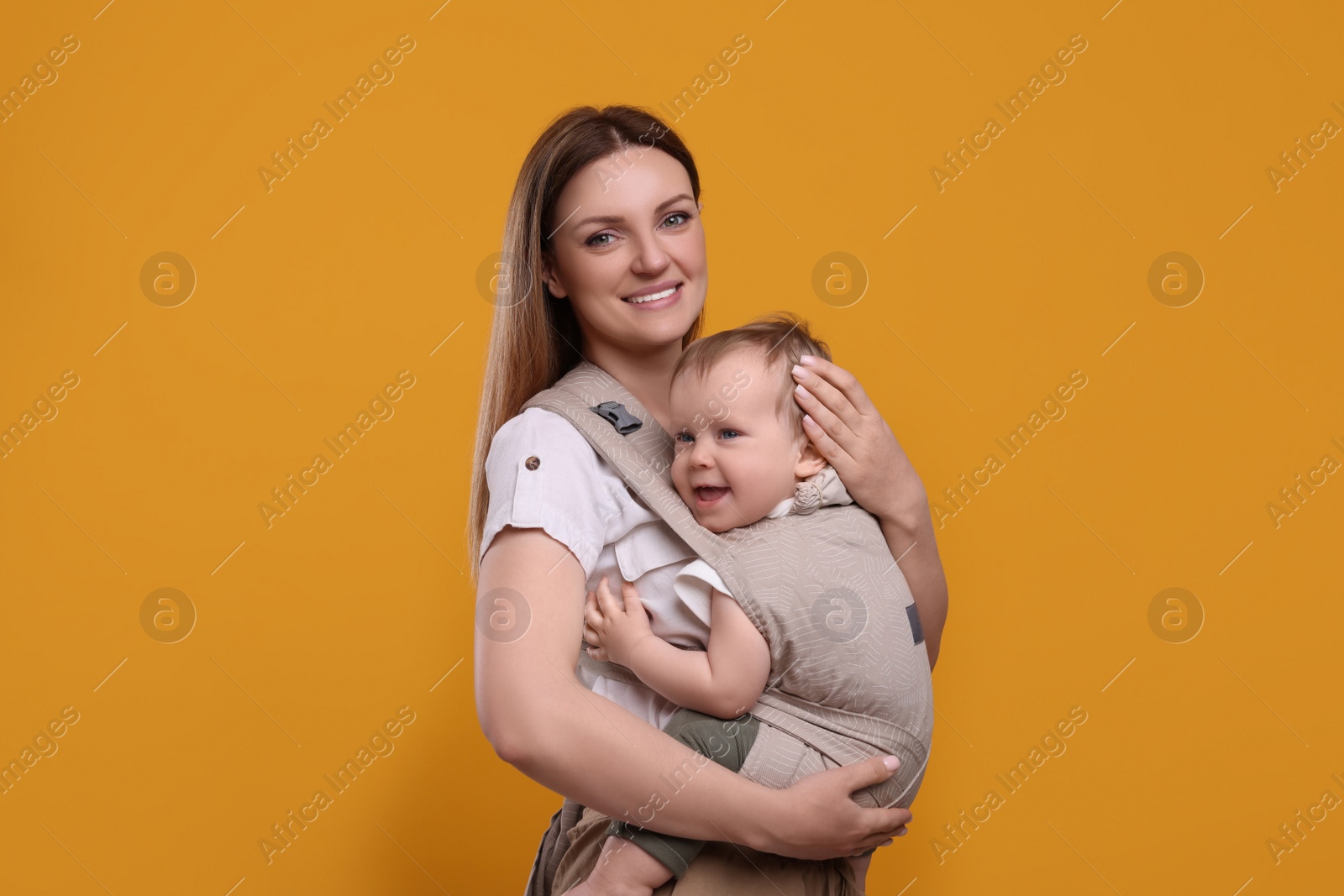 Photo of Mother holding her child in sling (baby carrier) on orange background