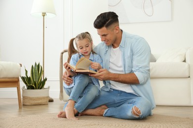 Photo of Father and his daughter reading book at home. Floor heating concept