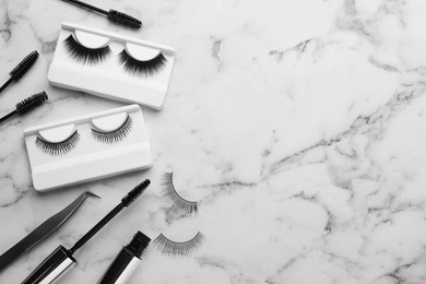 Flat lay composition with false eyelashes and tools on white marble table. Space for text