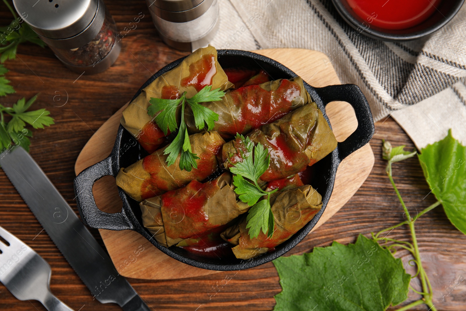 Photo of Delicious stuffed grape leaves with tomato sauce on wooden table, flat lay