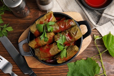 Photo of Delicious stuffed grape leaves with tomato sauce on wooden table, flat lay