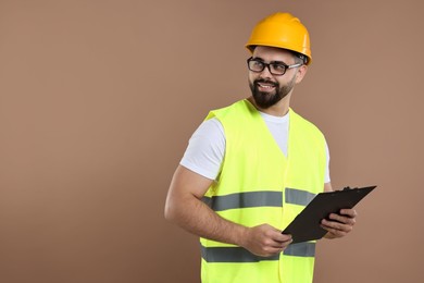 Engineer in hard hat holding clipboard on brown background, space for text