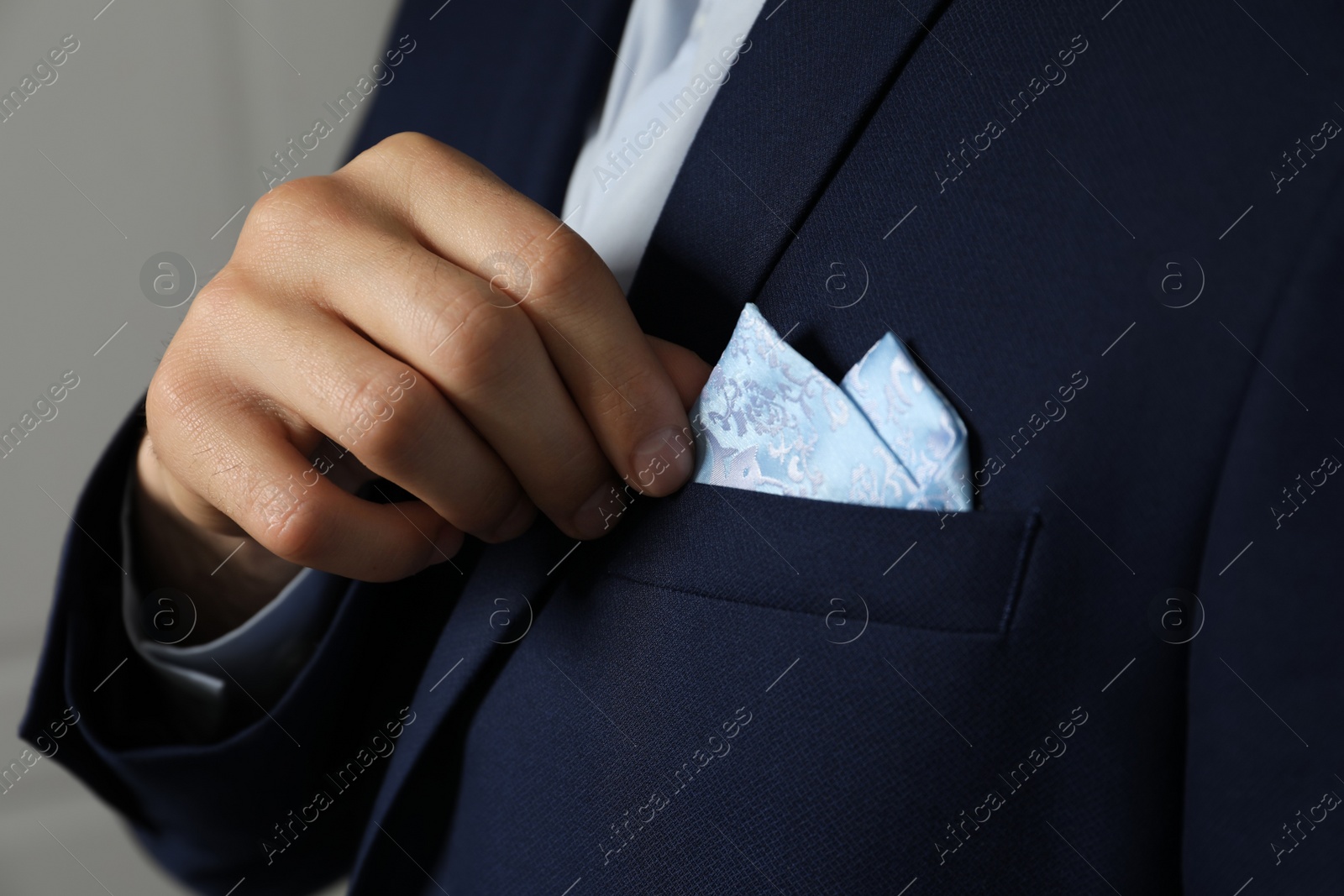 Photo of Man fixing handkerchief in breast pocket of his suit on light background, closeup