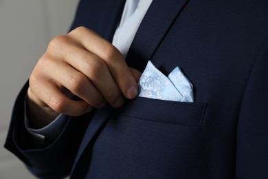 Photo of Man fixing handkerchief in breast pocket of his suit on light background, closeup