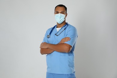 Photo of Doctor or medical assistant (male nurse) with protective mask and stethoscope on light grey background