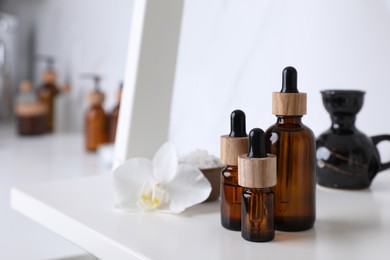 Photo of Bottles of essential oil on white shelf in bathroom. Space for text