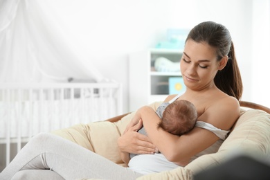Young woman breastfeeding her baby in nursery. Space for text