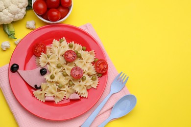 Photo of Creative serving for kids. Plate with cute hedgehog made of delicious pasta, sausages and tomatoes on yellow table, flat lay. Space for text