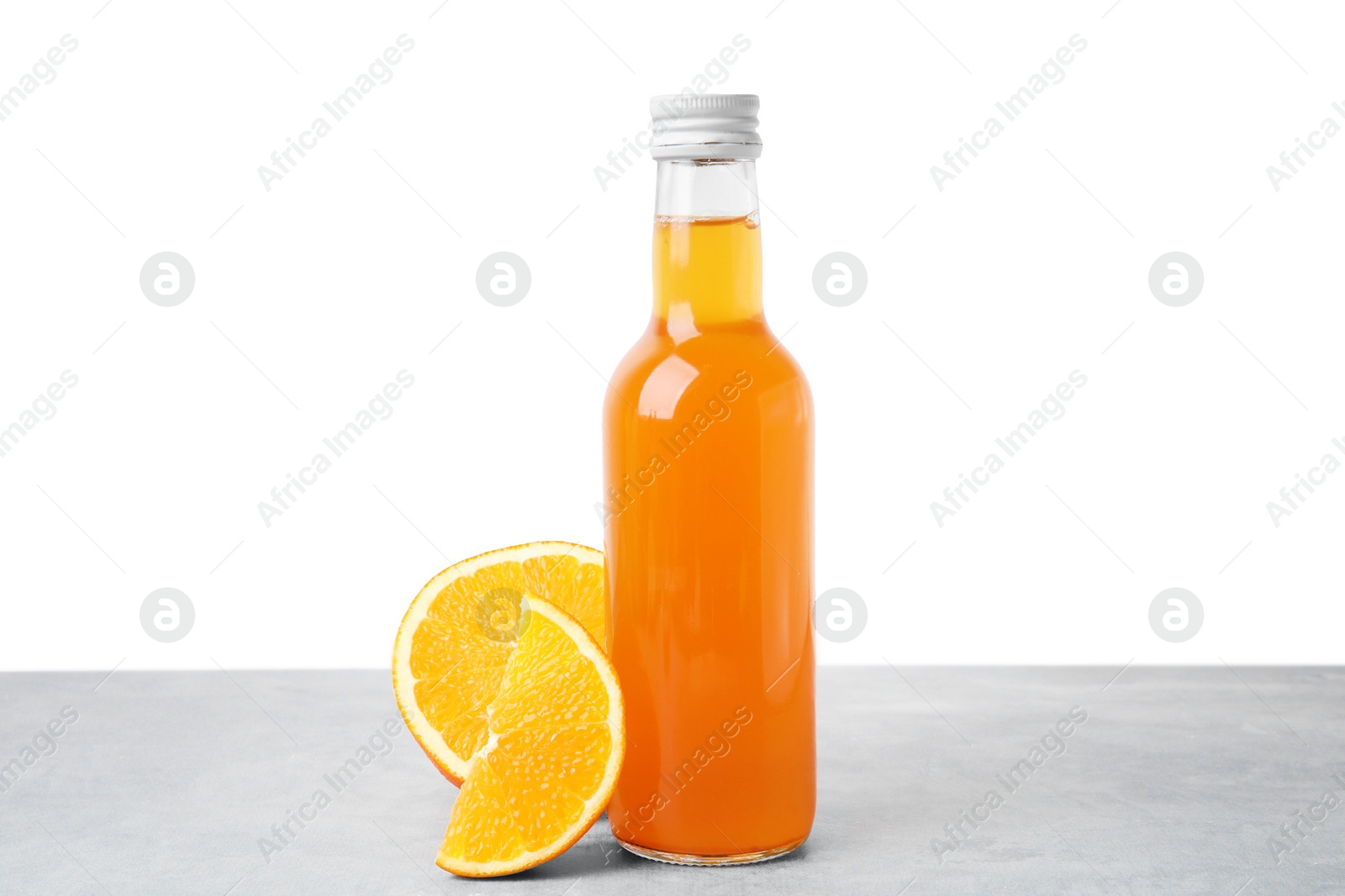 Photo of Delicious kombucha in glass bottle and orange on grey table against white background