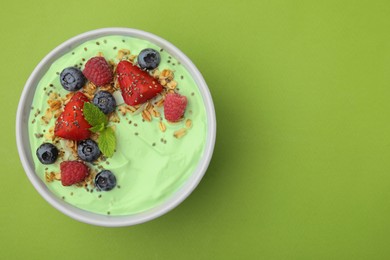 Tasty matcha smoothie bowl served with berries and oatmeal on green background, top view with space for text. Healthy breakfast