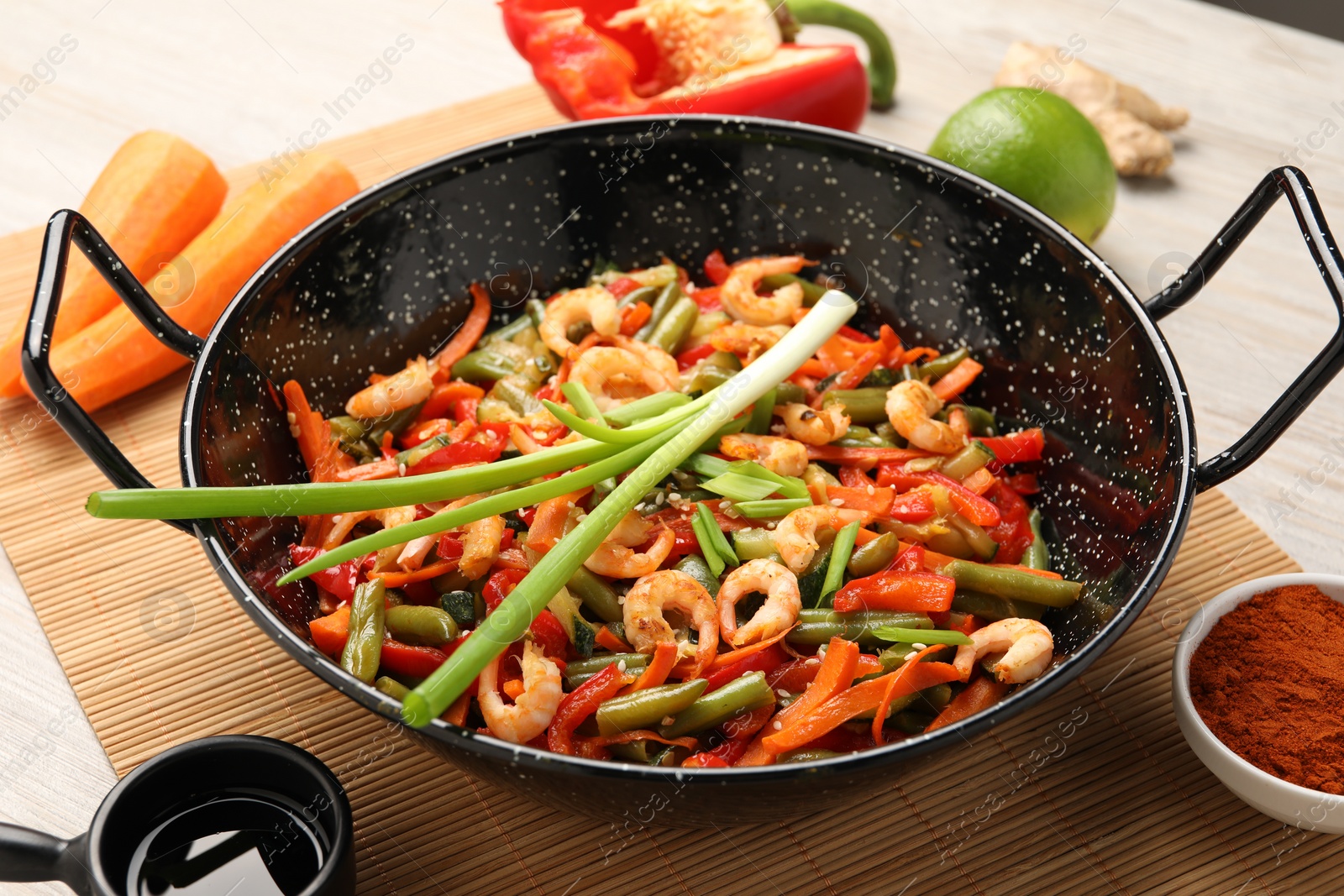 Photo of Shrimp stir fry with vegetables in wok and ingredients on wooden table