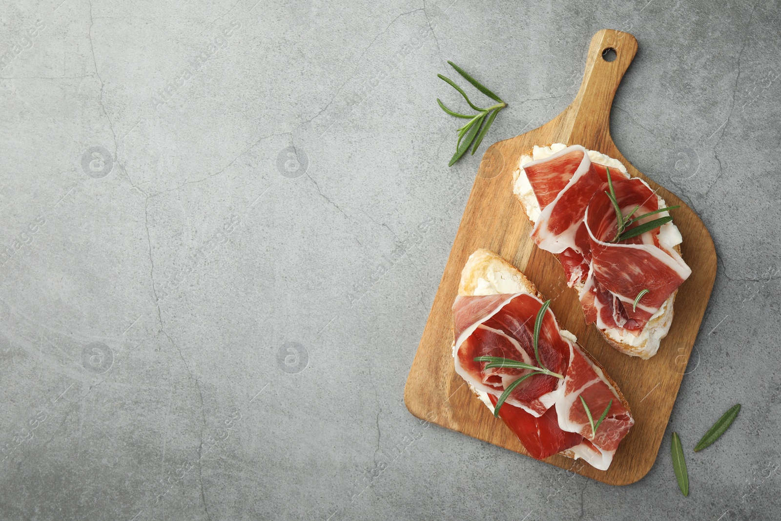 Photo of Tasty sandwiches with cured ham and rosemary on grey table, flat lay. Space for text