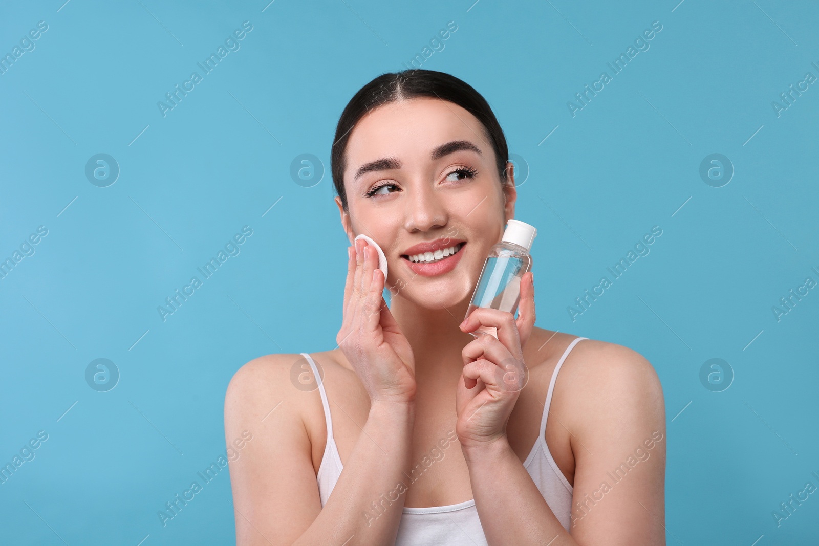 Photo of Beautiful woman removing makeup with cotton pad on light blue background