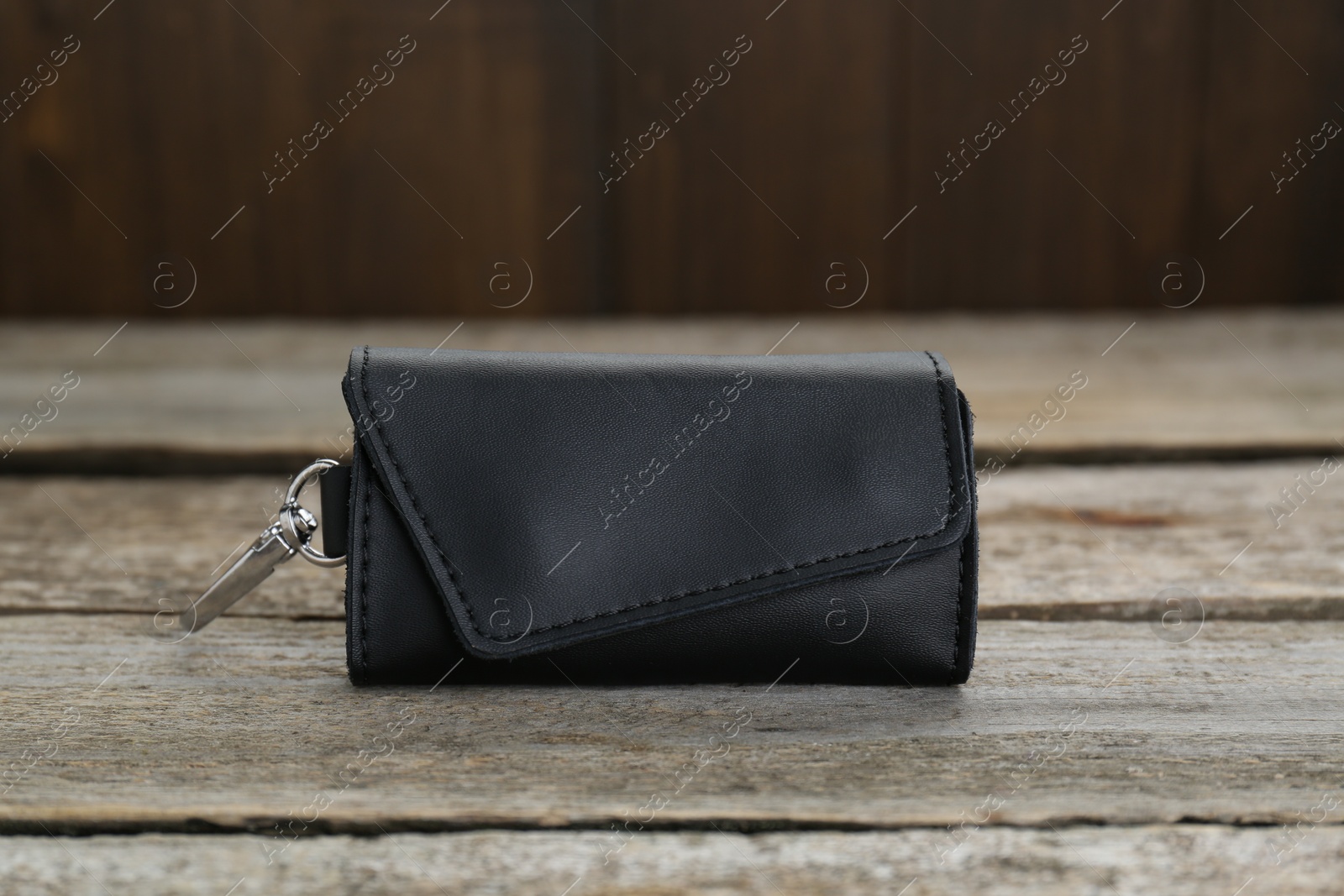 Photo of Stylish black leather keys holder on old wooden table, closeup