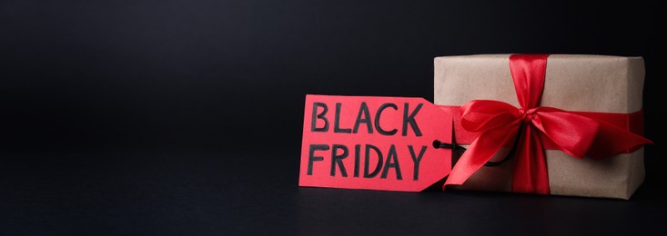Gift box and tag with words Black Friday on dark background, space for text