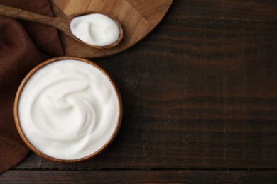 Delicious natural yogurt in bowl and spoon on wooden table, top view. Space for text