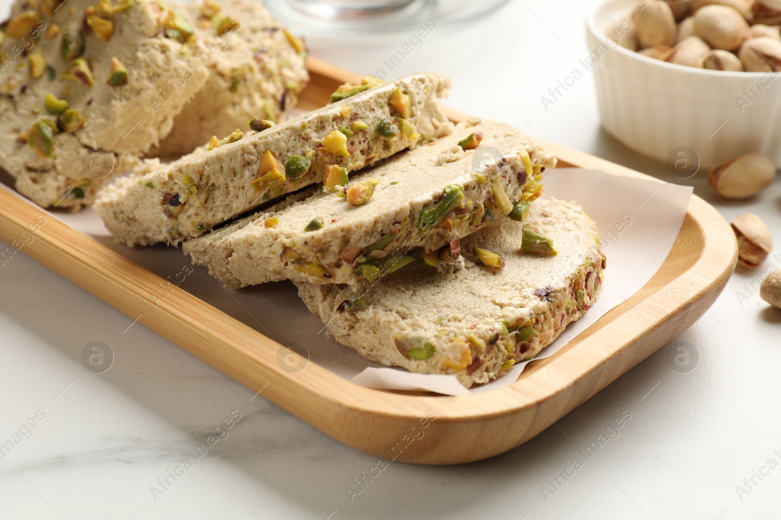 Photo of Tasty halva with pistachios on white marble table, closeup