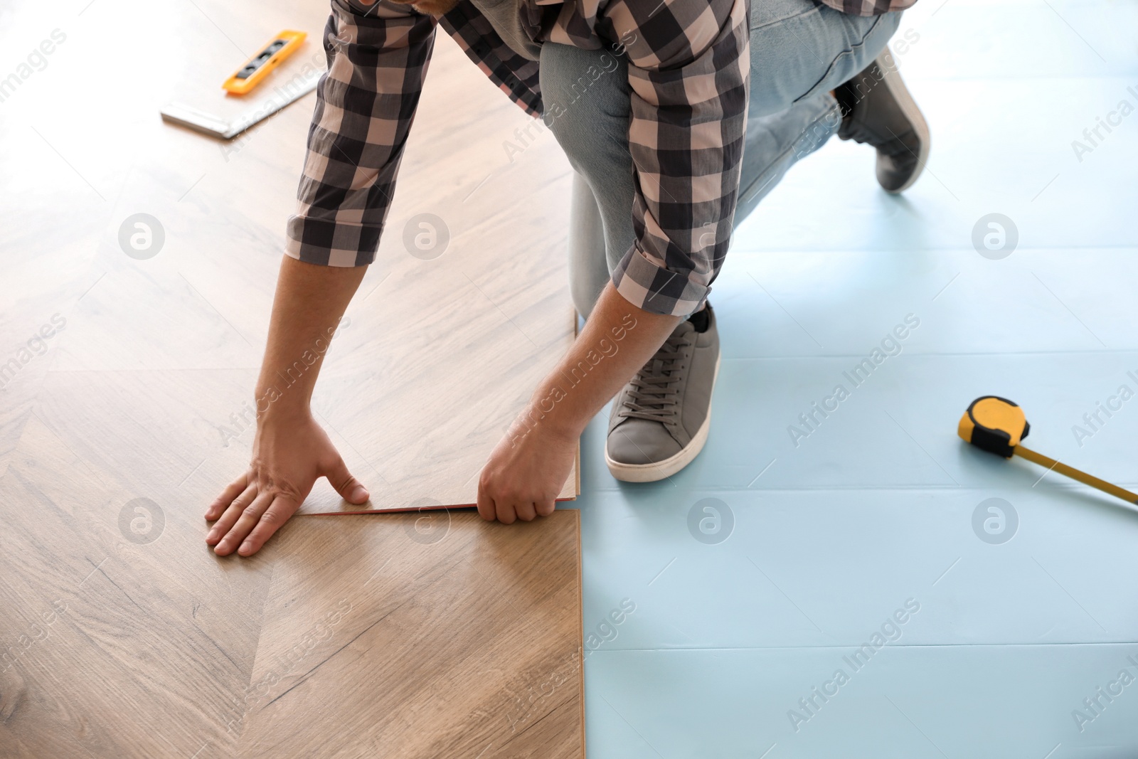 Photo of Worker installing laminated wooden floor indoors, closeup