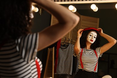 Photo of Young woman in mime costume putting beret near mirror indoors
