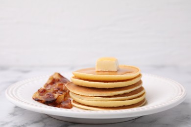 Photo of Delicious pancakes with butter, maple syrup and fried bacon on white marble table