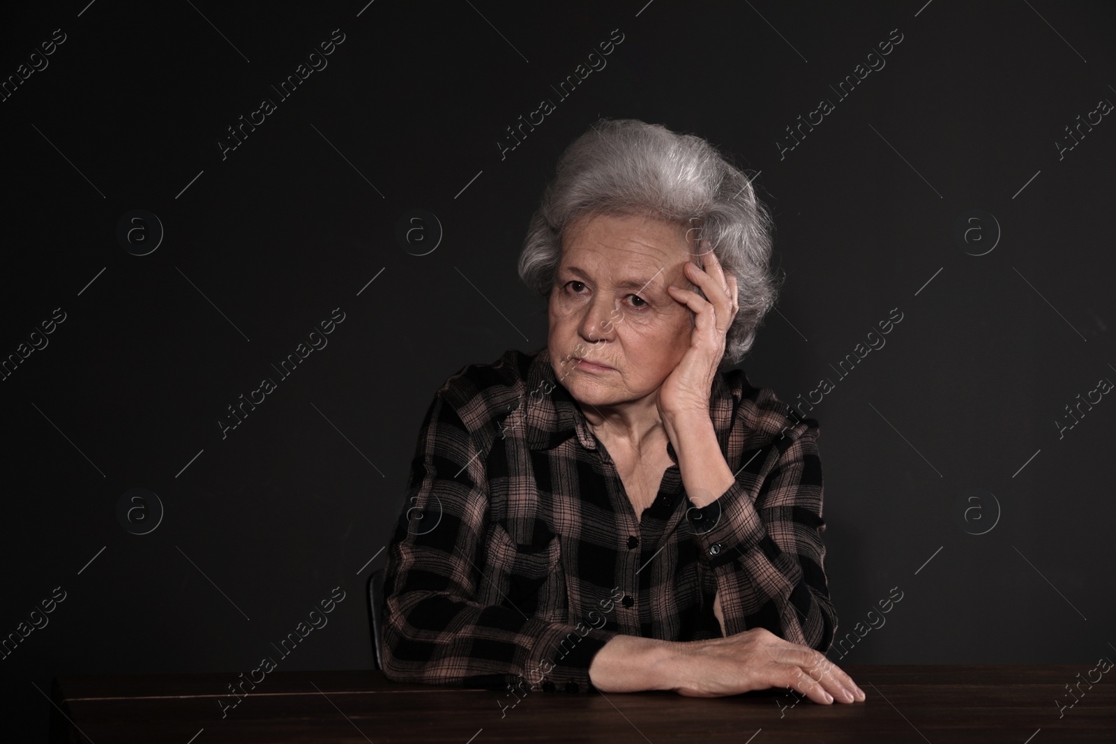 Photo of Poor upset woman sitting at table on dark background