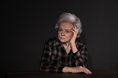 Photo of Poor upset woman sitting at table on dark background