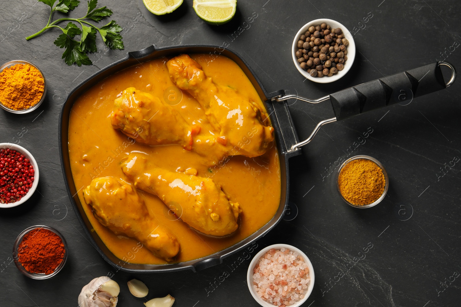 Photo of Tasty chicken curry and ingredients on black textured table, flat lay