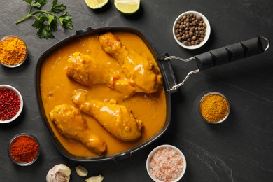 Tasty chicken curry and ingredients on black textured table, flat lay