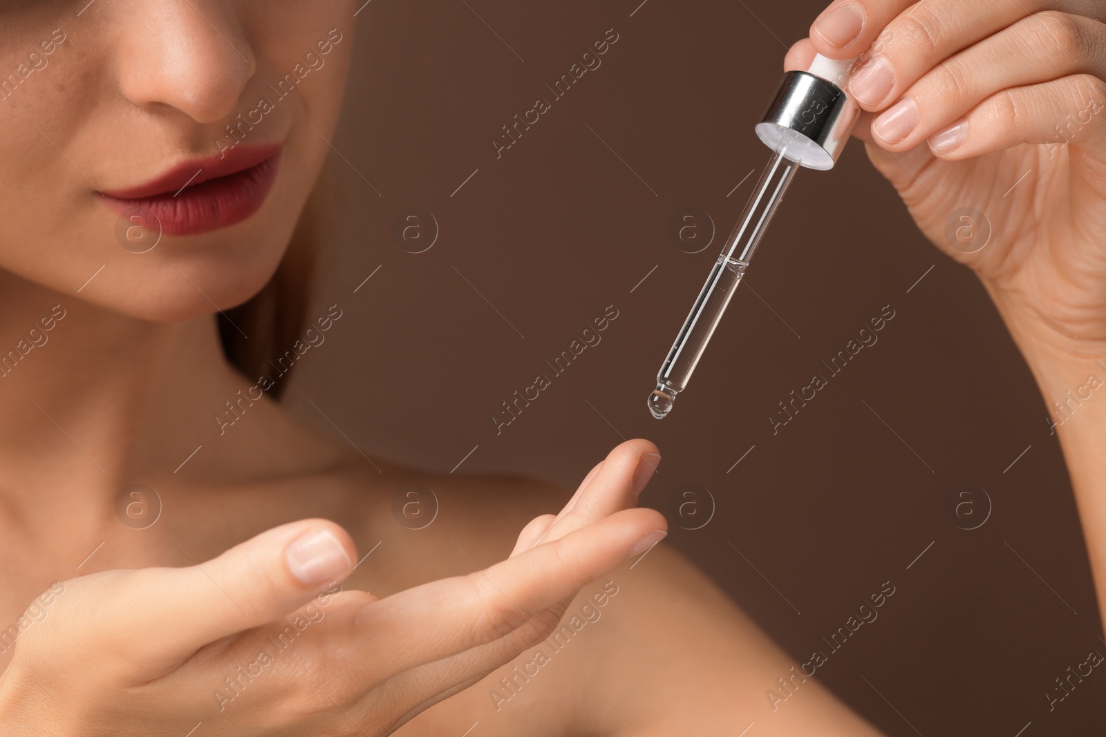 Photo of Beautiful young woman applying cosmetic serum onto her finger on brown background, closeup