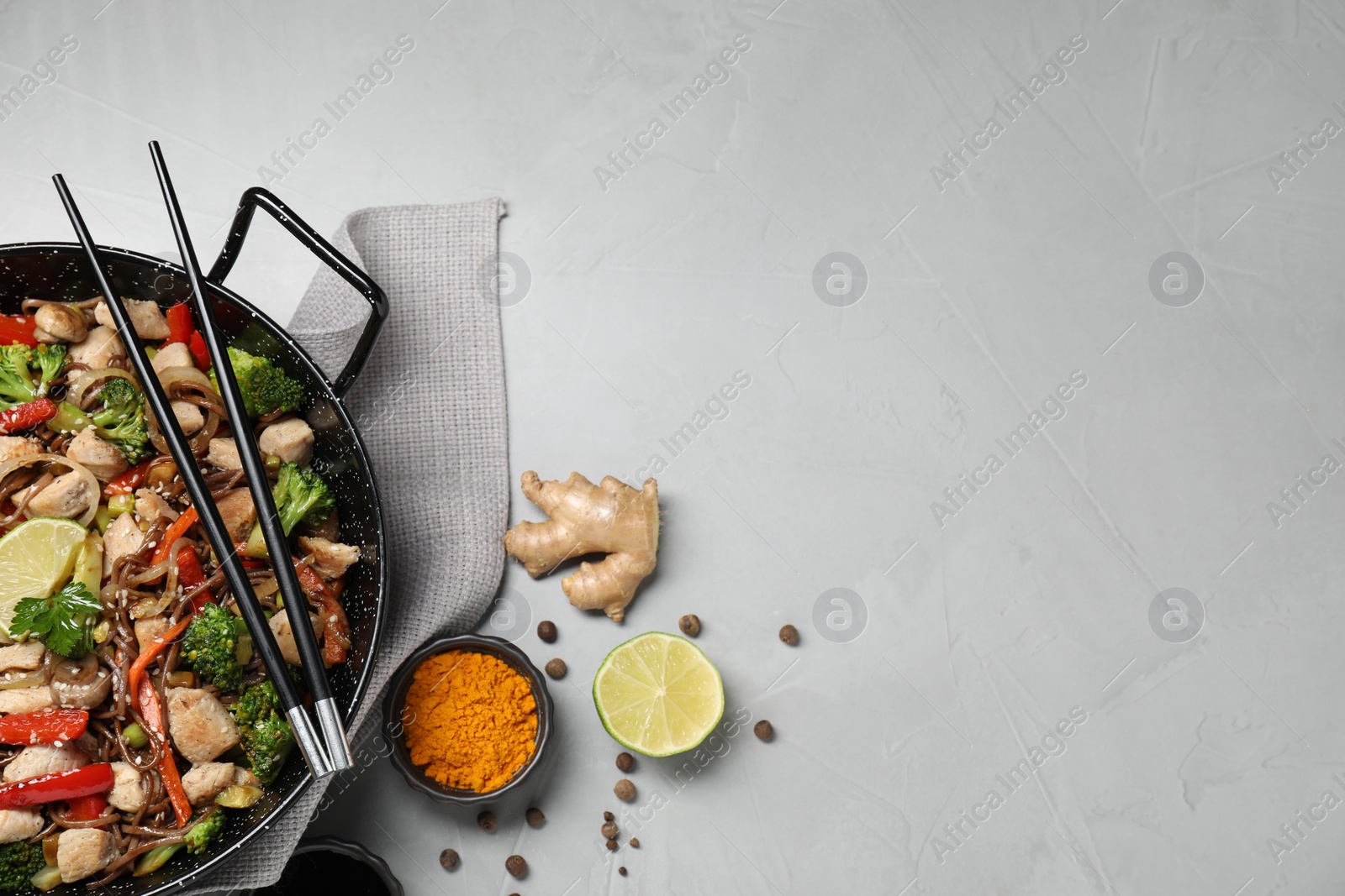 Photo of Stir-fry. Tasty noodles with meat in wok, chopsticks and ingredients on grey textured table, flat lay. Space for text