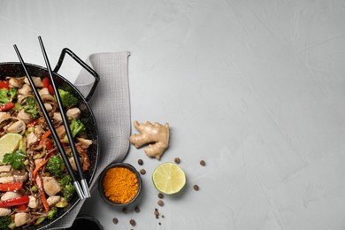 Photo of Stir-fry. Tasty noodles with meat in wok, chopsticks and ingredients on grey textured table, flat lay. Space for text