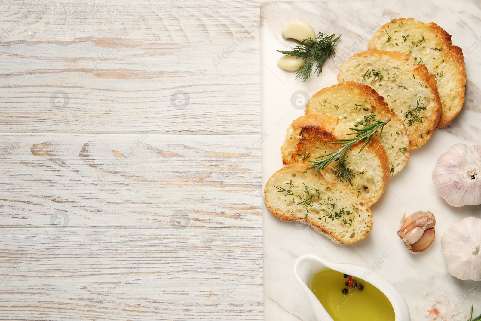 Photo of Tasty baguette with garlic, dill, rosemary and oil on white wooden table, top view. Space for text