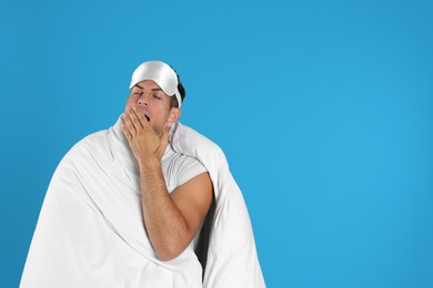 Man wrapped in blanket yawning on blue background. Space for text