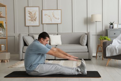 Overweight man stretching on mat at home